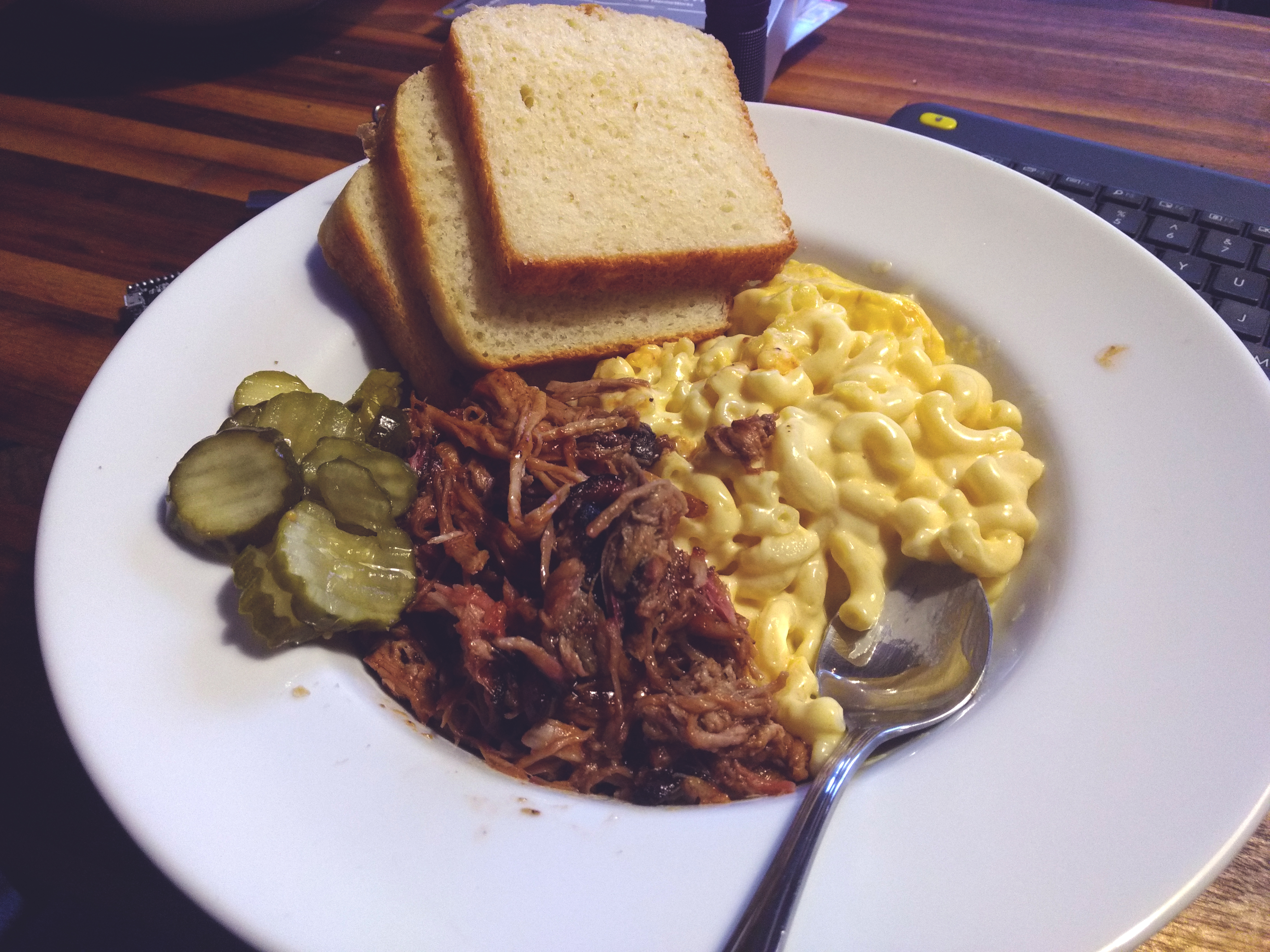 a plate of smoked pulled pork and macaroni and cheese with slices of home made bread and dill pickles