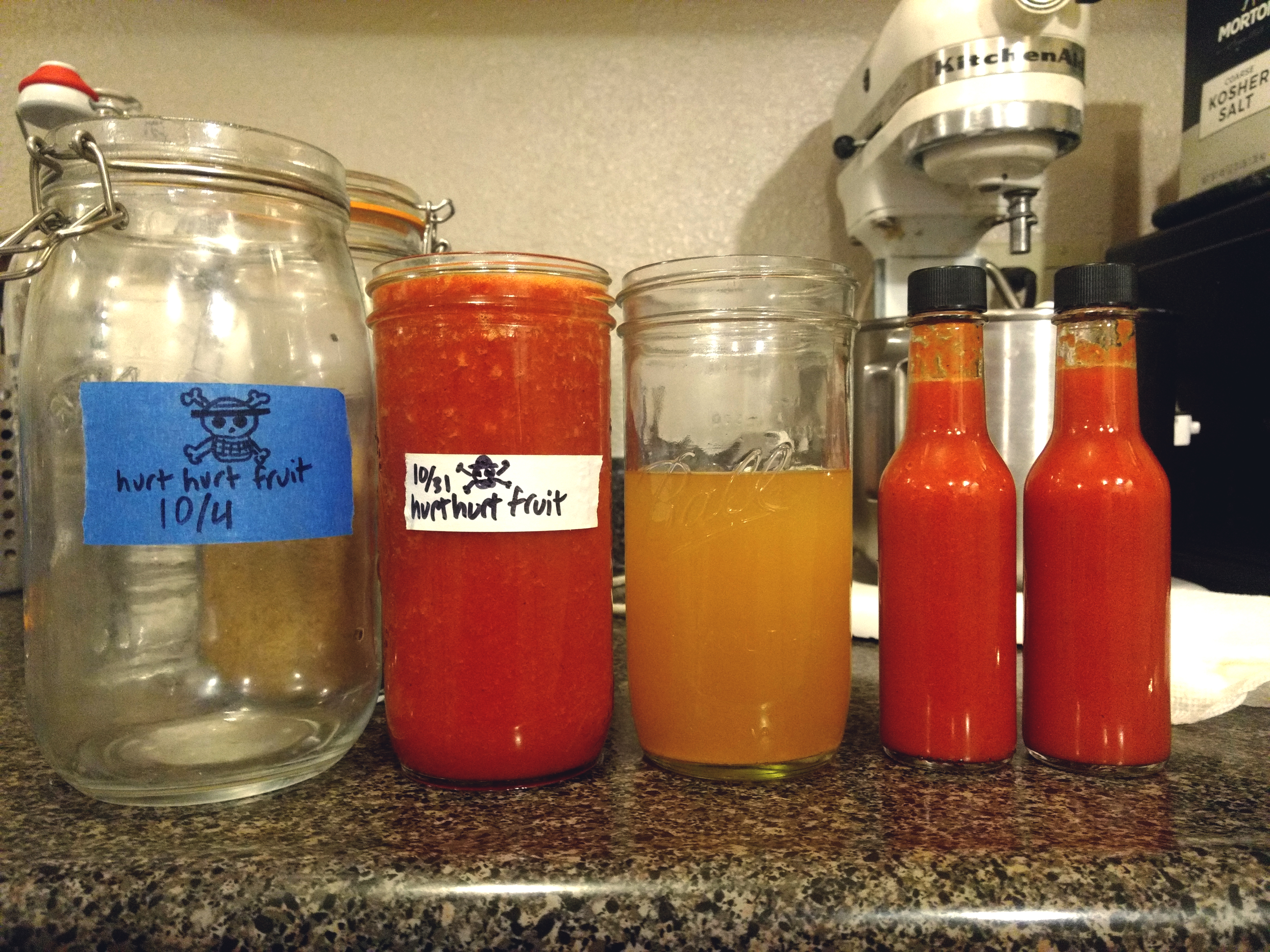 a jar of hot sauce sitting on a countertop next to a jar of brine and two hot sauce bottles